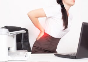 girl office worker holding her aching back from a chair, the concept of back pain in office workers, lactic acid in muscles and spinal problems, lumbago, osteochondrosis
