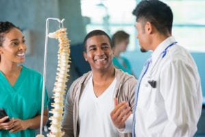 male doctor and female nurse with a male patient explaining using a model of the spine