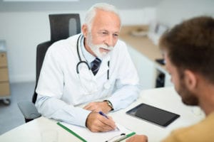 male doctor writing on a clipboard while on a male patient
