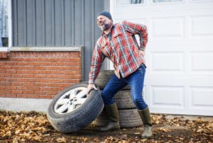 man straining and injuring his back lifting a large truck tire improperly