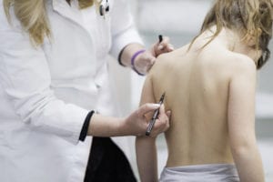 A physician examining a little girls back for scoliosis and marking it with a marker.