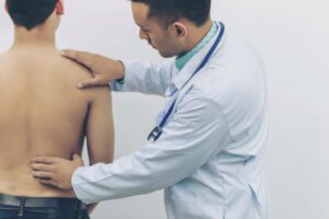 Doctor touches the back plate for causes of back pain with stethoscope on hospital. Concept of physical examination, medical and health care.
