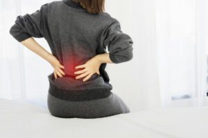 woman suffering from spinal stenosis sits on bed in bedroom in the morning