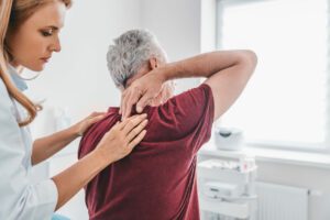 A female orthopedist is examining an elderly male patient’s back as part of scoliosis treatment for seniors.