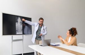 An orthopedic doctor discussing an X-ray on a computer and explaining a female patient's back pain problems in a medical clinic.