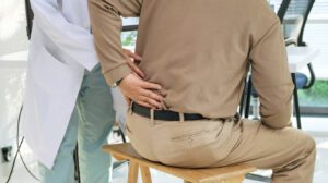 Doctor examining senior patient with back pain caused by herniated disc, during orthopedic checkup at hospital clinic.