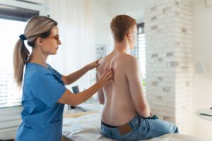 An orthopedist evaluates a teenage patient’s spine, posture, and potential spinal deformities related to scoliosis.
