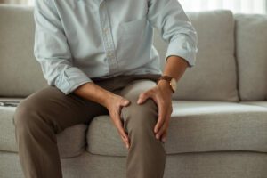 Young man sitting on the sofa is experiencing joint pain caused by osteoarthritis.