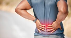 A man standing alone outside and suffering from back pain during his run.