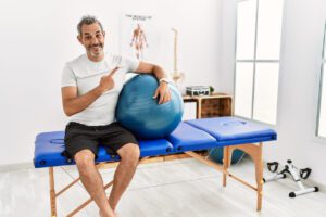 man at pain recovery clinic holding pilates ball cheerful with a smile on face